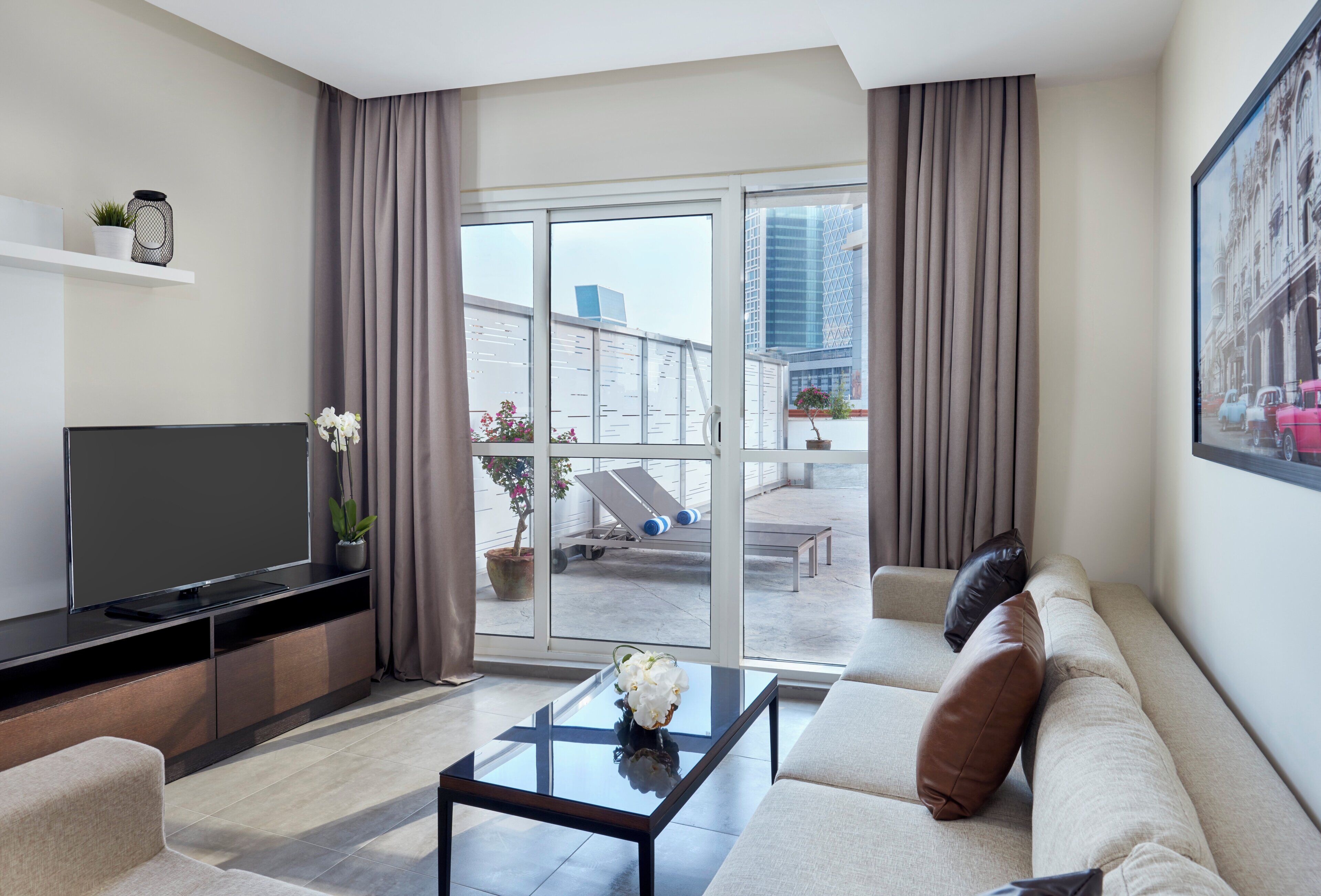 A modern living room with a flat-screen TV, a sofa, a coffee table, and a balcony with a view of the city.