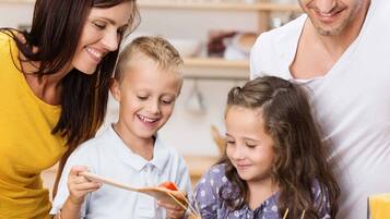 A family cooking together in a kitchen with a pot of spaghetti, a frying pan, and fresh tomatoes on the counter.