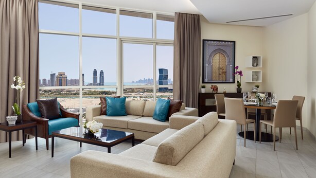 Ein modernes Wohnzimmer mit großem Fenster und Blick auf die Stadt, einem Essbereich mit Tisch für zwei Personen sowie einem dekorativen Wandbild.
