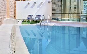 A modern pool area with clear blue water, metal pool ladders, and two lounge chairs with blue cushions. - Staybridge Suites Doha Lusail by IHG (Doha)