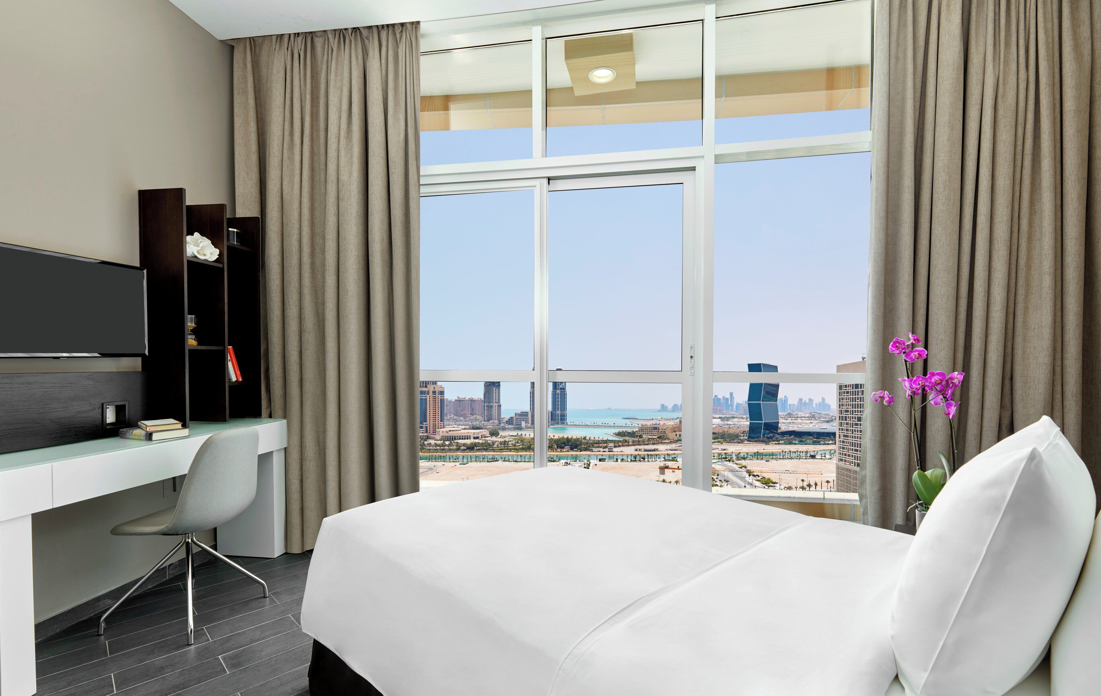 Une chambre d’hôtel équipée d’un lit, d’un bureau, d’une chaise, d’une télévision et offrant une vue sur le paysage urbain.