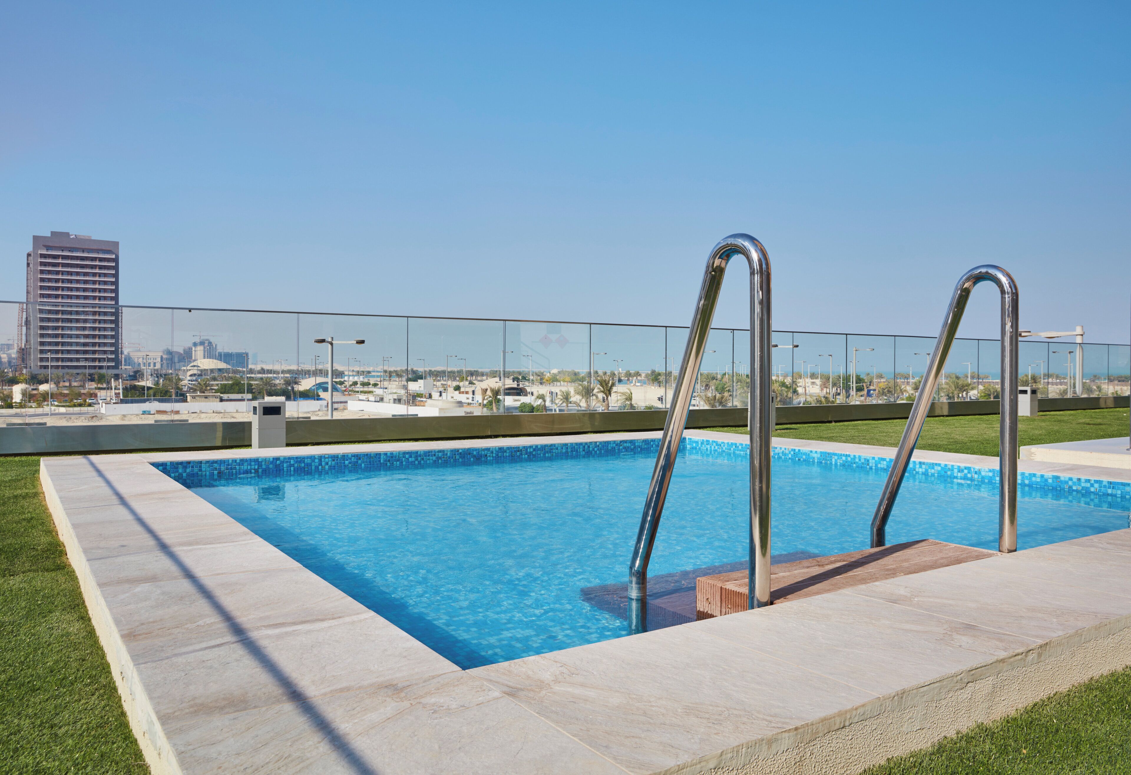 Une piscine dotée de deux échelles en métal, entourée d’une terrasse carrelée et d’une zone herbeuse.