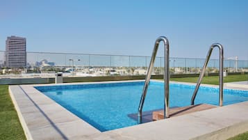 Une piscine dotée de deux échelles en métal, entourée d’une terrasse carrelée et d’une zone herbeuse.