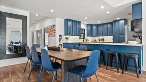Une cuisine moderne avec des meubles de rangement bleus, une table à manger en bois avec des chaises bleues et un coin bar avec des tabourets.