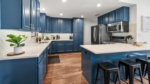 Une cuisine moderne avec des meubles bleus, un grand îlot central, des appareils électroménagers en acier inoxydable et un revêtement de sol en bois.