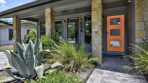 Un bâtiment avec des piliers en pierre, le numéro « 1006 » au-dessus de la porte, et un petit jardin avec des plantes et des fleurs.