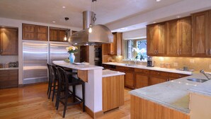 Une cuisine moderne avec des meubles en bois, des appareils électroménagers en acier inoxydable et un îlot central doté de tabourets de bar.