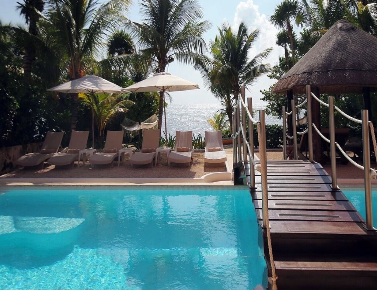 A poolside area with lounge chairs and umbrellas, a wooden deck, and palm trees.