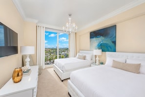 A hotel room with two beds, a TV, a chandelier, and a painting.