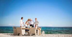 A group of people dining at a beachside table with a view of the ocean.