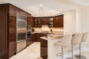 A modern kitchen with dark wood cabinets, stainless steel appliances, a marble countertop, and a bar area with stools.