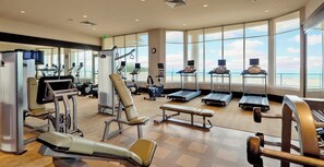 A spacious gym with various exercise equipment, large windows offering a view of the beach, and a modern interior design.
