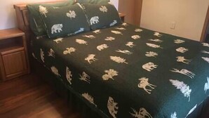 Een bed met een donkergroene spreidek met witte dierenprints, een houten nachtkastje en een houten vloer.