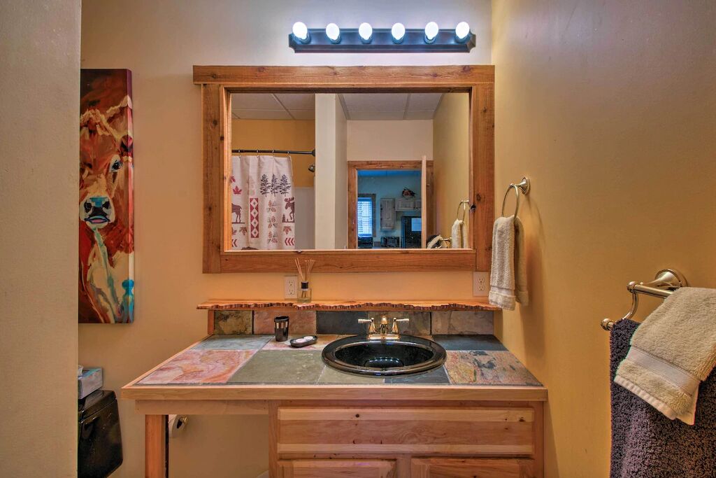 A bathroom with a wooden vanity, a black sink, a mirror with lights, and a towel rack.