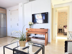 Un salon moderne avec un téléviseur à écran plat fixé au mur, un meuble en bois, une table basse en verre et une plante en pot.