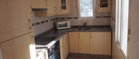 A kitchen with wooden cabinets, a microwave, a sink, and a window.