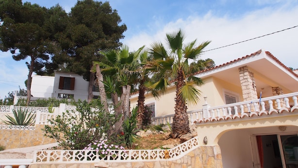 A house with a stone facade, a balcony with white balustrades, and a palm tree in the garden.