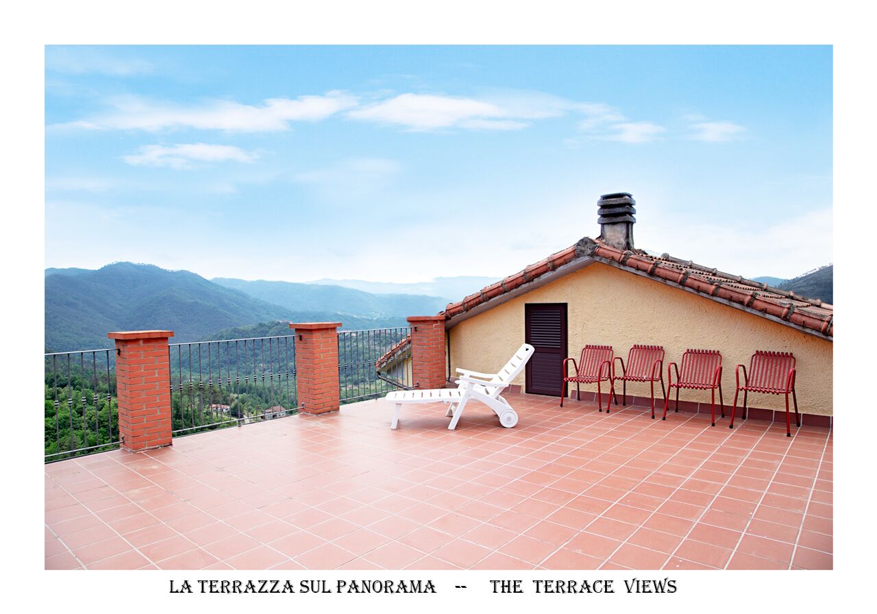 A terrace with a view of mountains, a tiled floor, a white lounge chair, and red chairs.