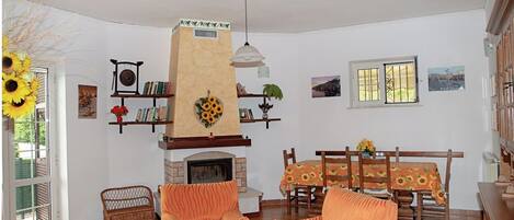 A living room with a fireplace, wicker furniture, and a dining area with a table and chairs.