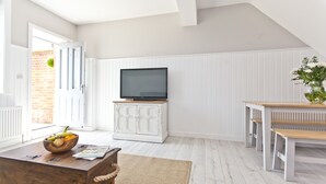 A modern living room with a television on a cabinet, a wooden coffee table with a bowl of fruit, and a bench. - Seaside Cottage with panoramic sea views. (Bournemouth)