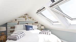 A bedroom with a sloped ceiling, skylight windows, a bed with white bedding, and a wooden headboard. - Seaside Cottage with panoramic sea views. (Bournemouth)
