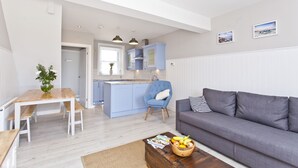 A modern living room with a grey sofa, a wooden coffee table with fruit, a blue armchair, and a kitchen in the background. - Seaside Cottage with panoramic sea views. (Bournemouth)