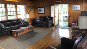 A cozy living room with wooden walls and floors, two dark sofas, a wooden coffee table, and a ceiling fan. - Lakeside Adirondack Lodge (Tupper Lake)