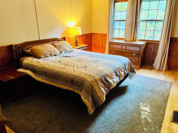 A bedroom with a bed, wooden nightstands, a dresser, and a window with curtains. - Lakeside Adirondack Lodge (Tupper Lake)