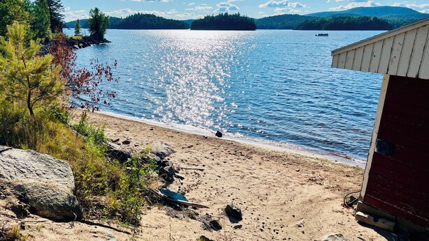 A beach with a wooden structure, a rocky shoreline, and a clear view of a lake. - Lakeside Adirondack Lodge (Tupper Lake)