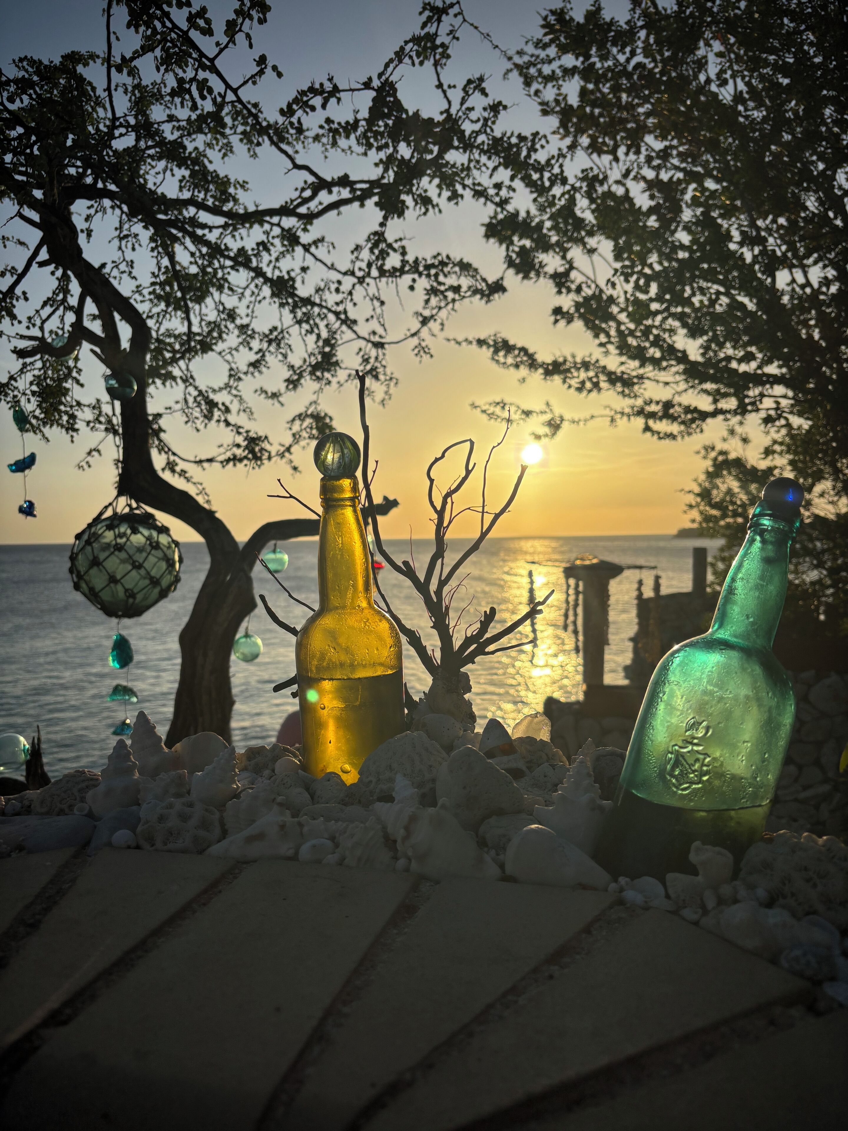 A sunset view with bottles and a hanging ornament on a rocky shore.