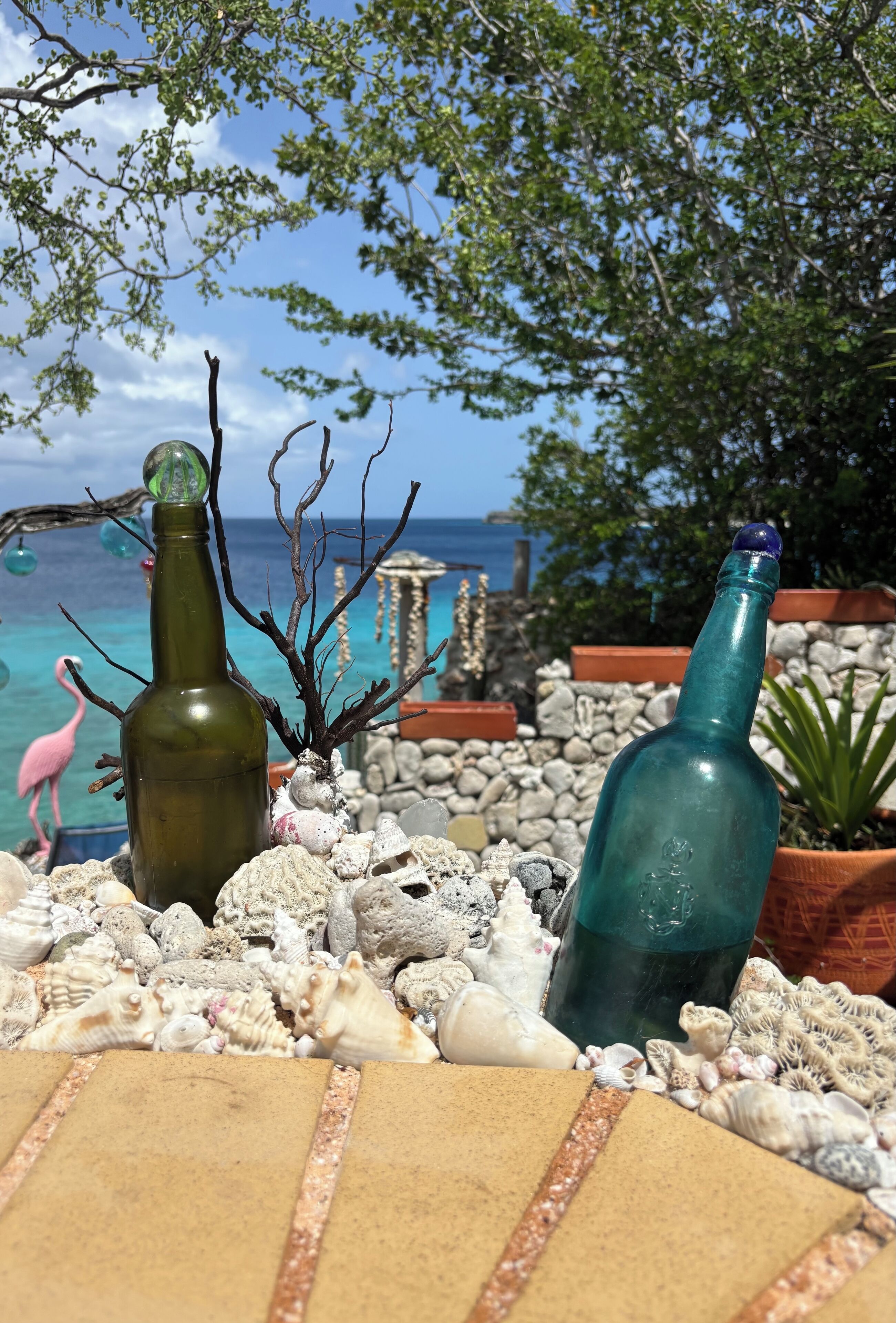 A beach setting with two green bottles, a flamingo, and various shells.