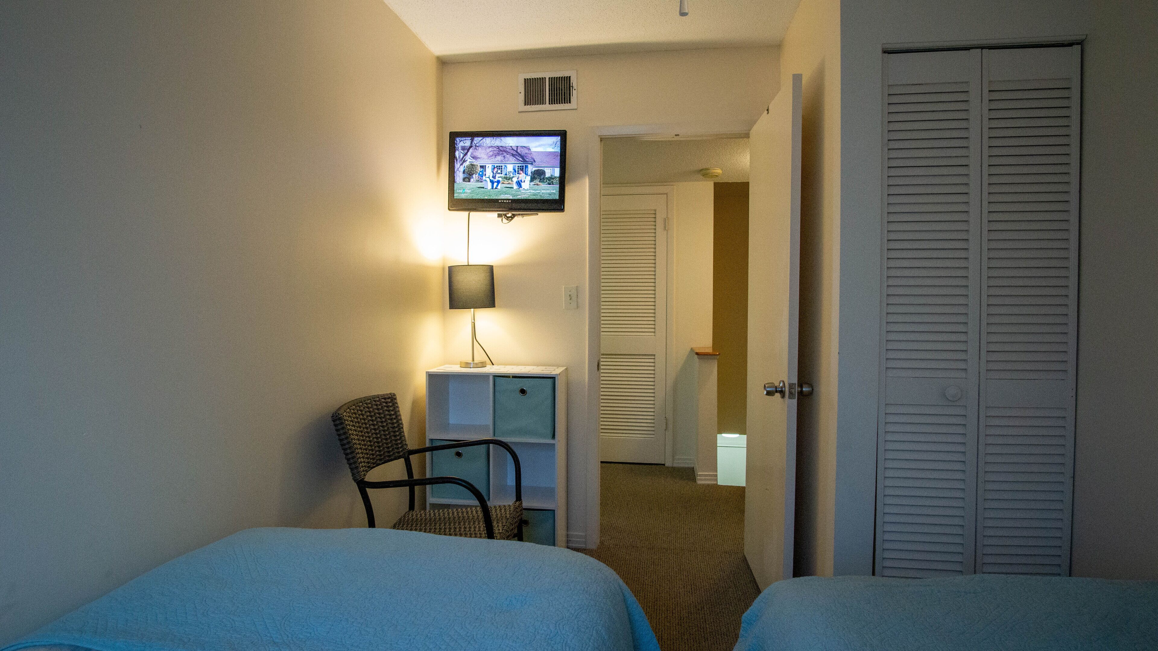 Une chambre d’hôtel avec deux lits, un bureau avec une lampe, un téléviseur fixé au mur et un placard.