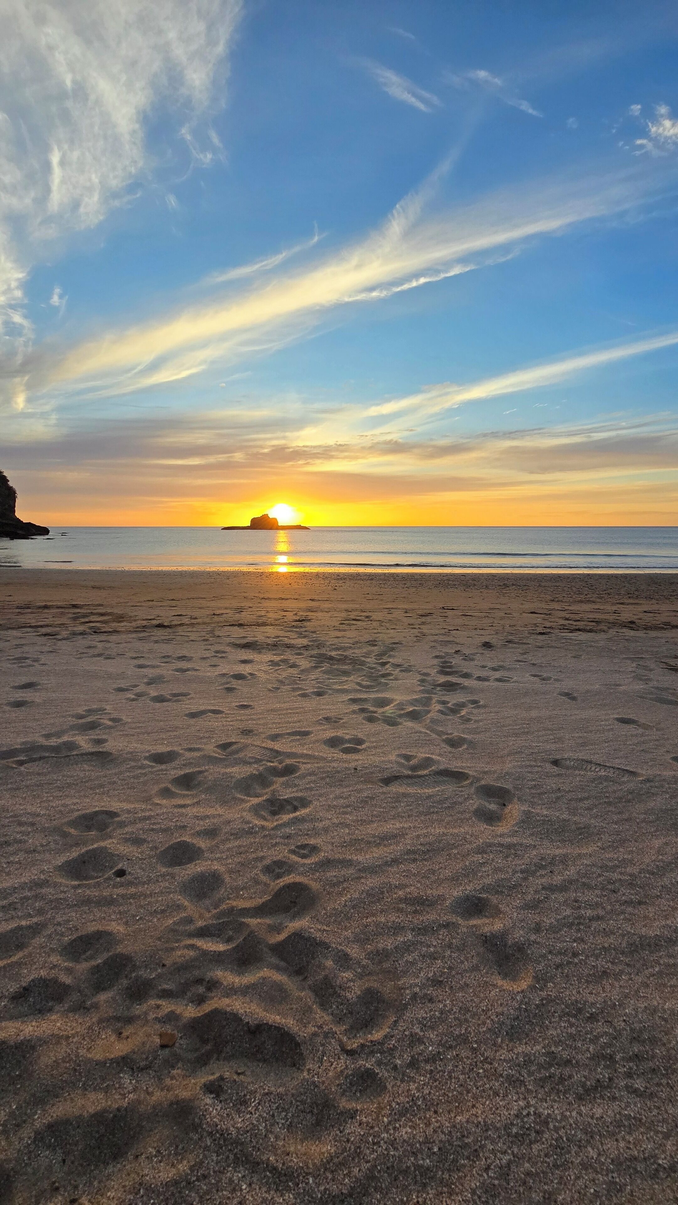 Une plage parsemée d'empreintes et un coucher de soleil en arrière-plan.