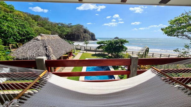 Una hamaca con vista a una piscina y al océano, con una estructura de techo de paja.