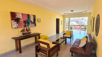 A living room with yellow walls, a wooden coffee table, a brown leather sofa, and a yellow armchair. There is a large abstract painting on the wall and a small ship model on a wooden table.