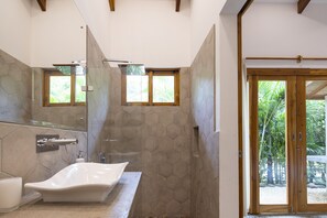 A bathroom with a freestanding bathtub, a glass-enclosed shower, and a view of the outdoors through a wooden door.