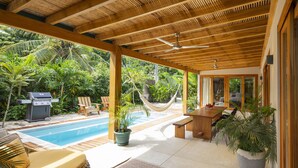 Un espacio al aire libre cubierto con piscina, muebles de madera y plantas en macetas.