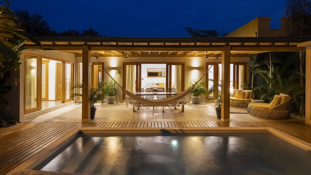 Un área de piscina con una hamaca, asientos y un comedor con vista al interior.