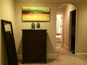 Un corridoio con un'ampia cassettiera in legno scuro, un grande quadro astratto appeso sopra e uno specchio appoggiato al muro.