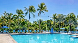 A swimming pool with lounge chairs and umbrellas, surrounded by palm trees. - Keys Waterfront Condo: Beach, Pool & Sunset Views! (Tavernier)