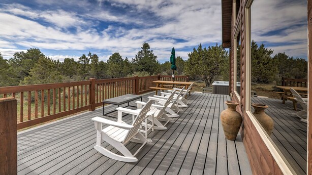 A wooden deck with white rocking chairs and a table, overlooking a forested area.