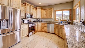 A kitchen with wooden cabinets, stainless steel appliances, a granite countertop, and a large window offering a view.