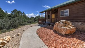 A wooden cabin with a porch, a large rock in front, and a gravel path leading to the entrance.