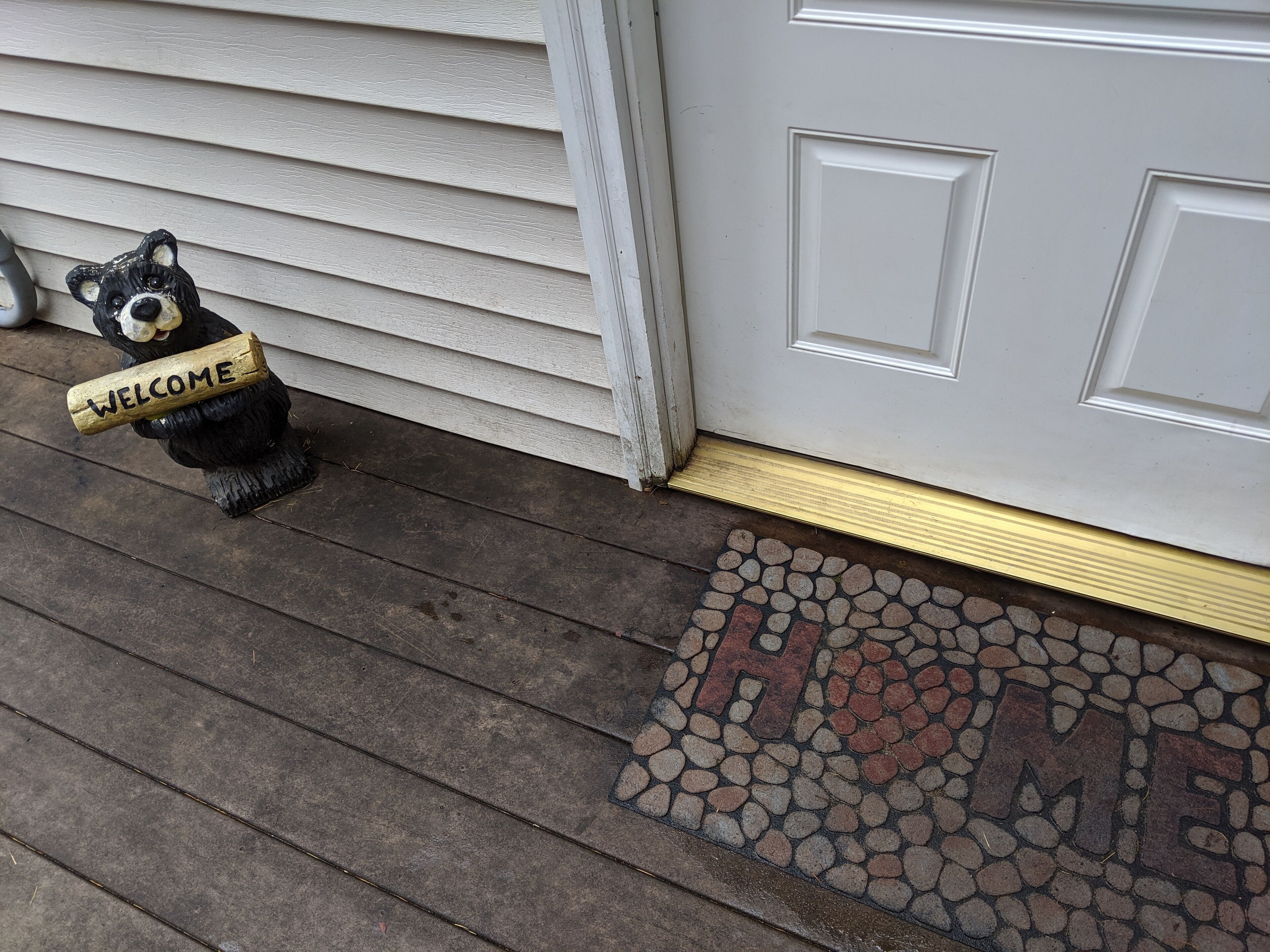 A black bear figurine holding a 'WELCOME' sign on a wooden porch.