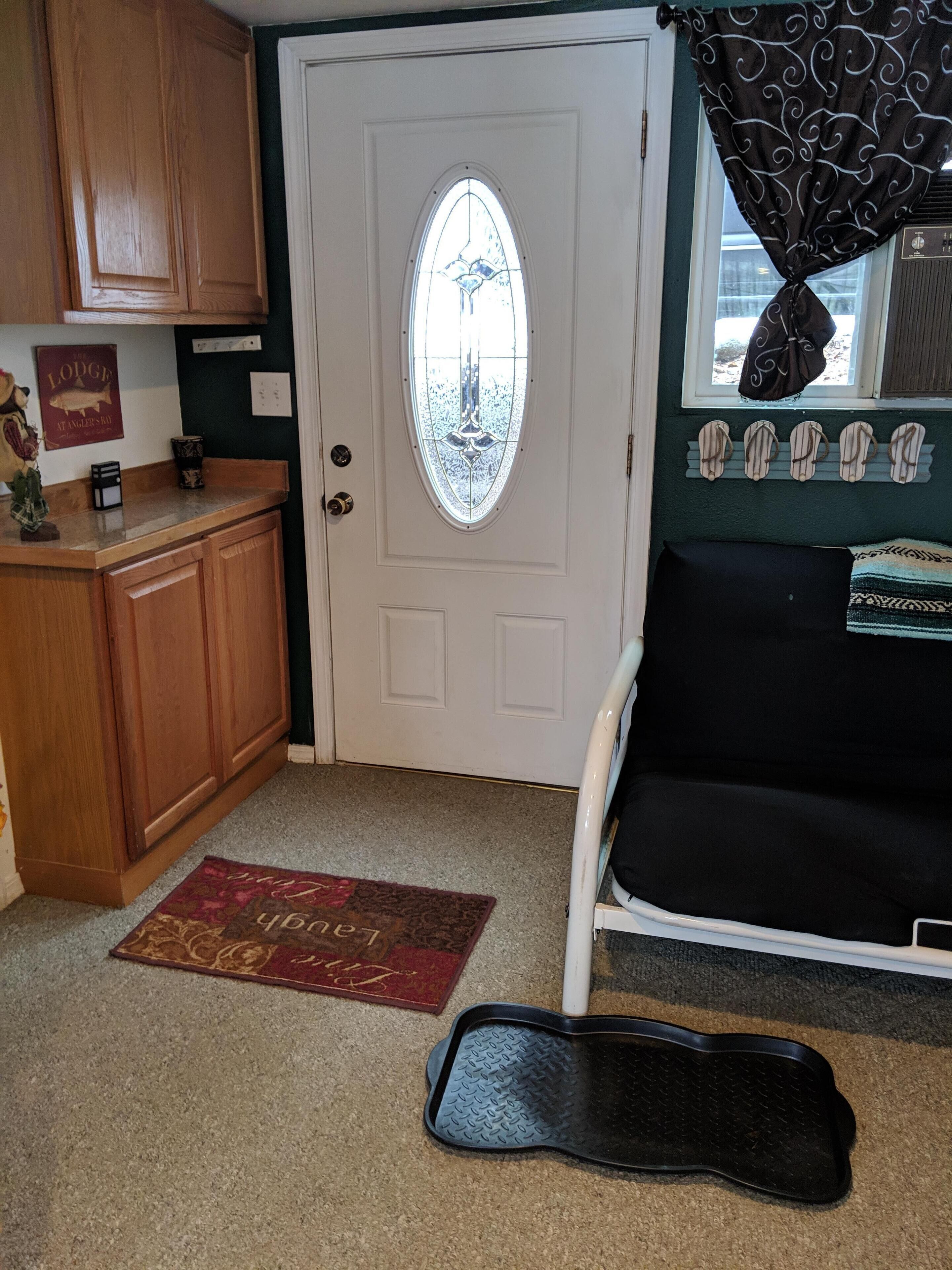 A compact living space with a white door, a small kitchenette with wooden cabinets, a black couch, and a patterned rug on the floor.