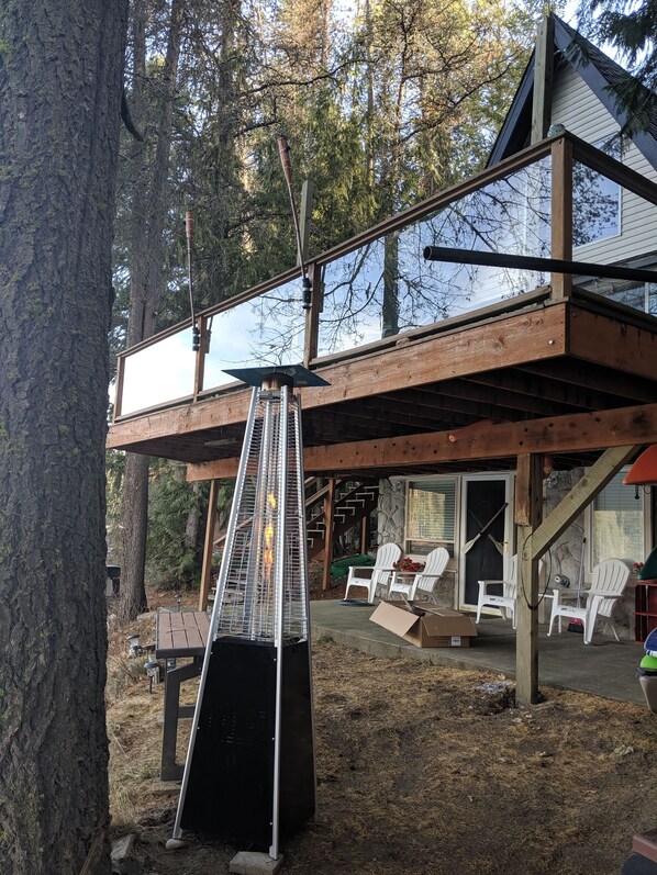 A wooden deck with a metal grill, white chairs, and a stone wall.
