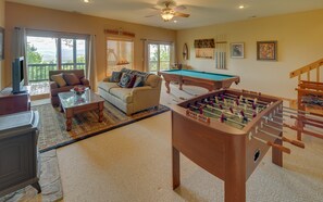 A spacious living room with a pool table, a foosball table, a sofa, and a television.