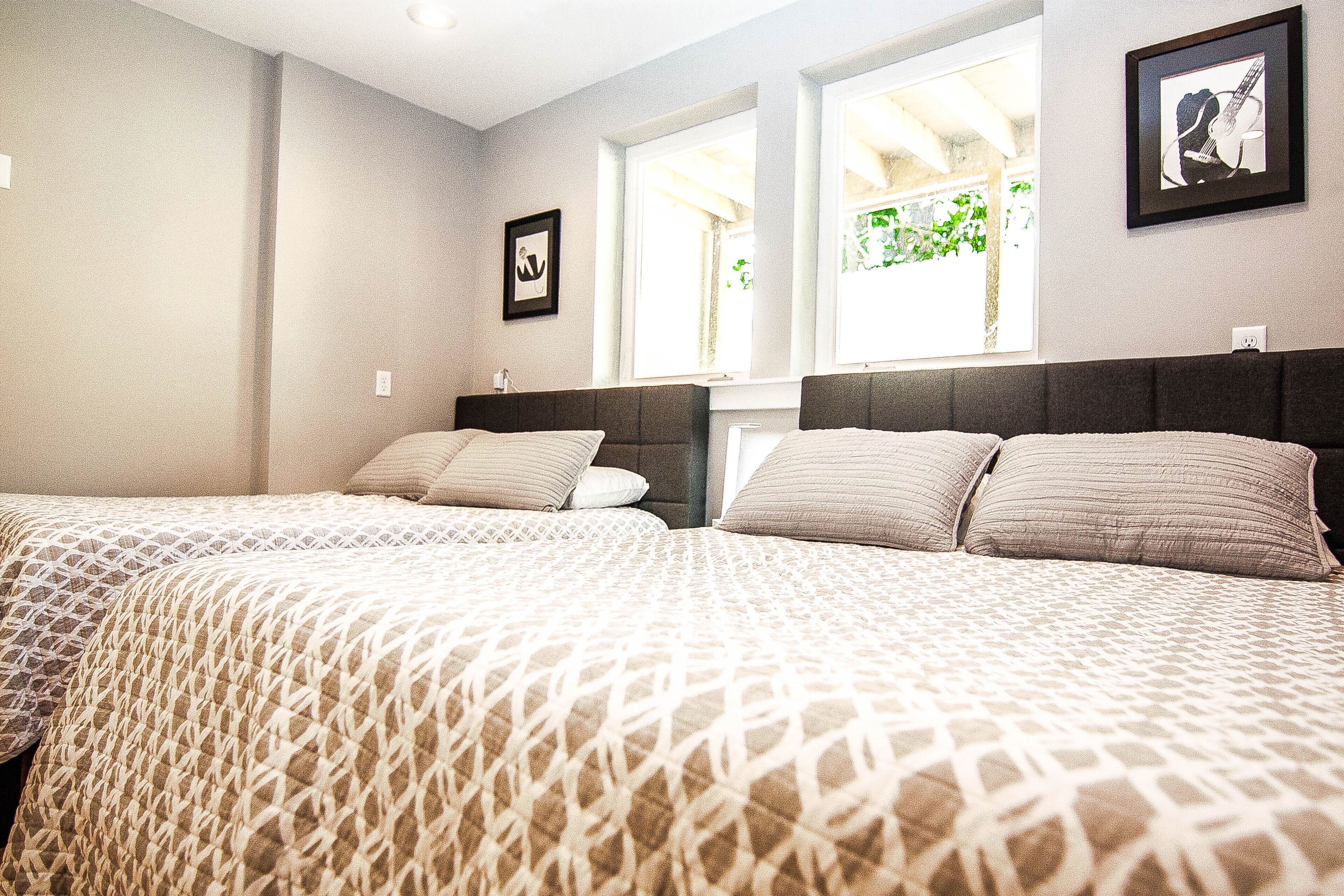 A hotel room with two beds, a window with a view of greenery, and a framed picture on the wall.