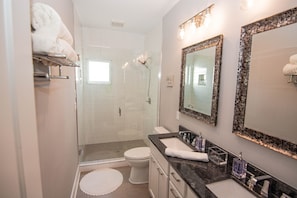 A modern bathroom with a glass shower enclosure, a white toilet, and a vanity with a black countertop.