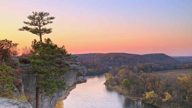 A river with a rocky cliff and a lone tree on top.